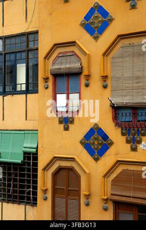 Vibrant yellow house facade in Girona, Catalonia, featuring arched windows, wooden shutters, woven blinds, blue geometric ceramic tiles, and decorativ Stock Photo