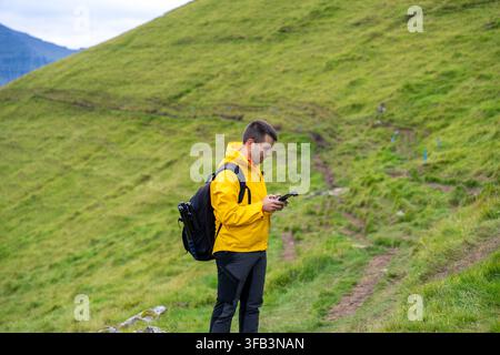 Man hiking Kalsoy Island checking mobile device connected to a remote control to fly a drone Stock Photo