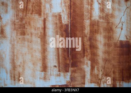 A close-up texture of a heavily weathered and rusted metal surface featuring vertical streaks of brown oxidation over faded, peeling paint. Stock Photo
