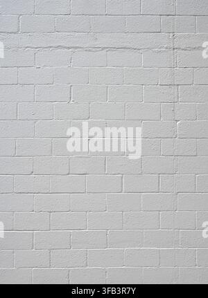Vertical view of painted white cinder block wall surface with flat CMU texture, porous, rough blocks and one repaired row Stock Photo