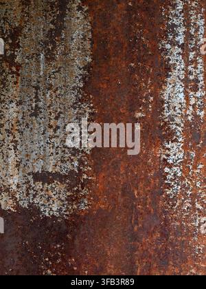 Vertical view of rusted metal surface with worn white paint, exposed iron sheet metal, oxidized pitted corrosion, and rust stained texture Stock Photo