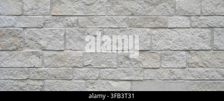 Horizontal view of sawn rock brick and mortar wall surface with rough cut white stones, uneven rectangular blocks and porous matching mortar Stock Photo