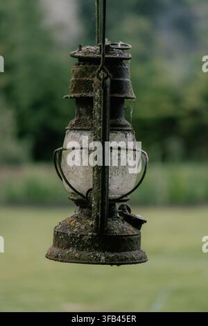 Heavily rusted antique kerosene lantern covered with moss, lichen and cobwebs hanging outdoors Stock Photo