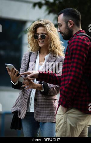 Casual outdoor meeting between two friends engaging with technology as they share a smartphone device, creating a moment of connection, teamwork, and Stock Photo