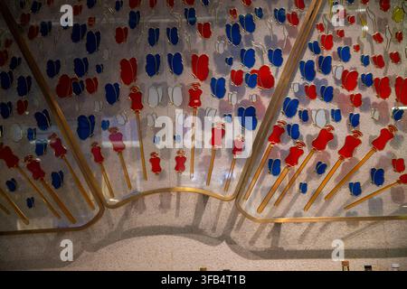 An indoor decorative glass wall panel featuring dozens of small red, blue, and white stained-glass butterfly and flower motifs accented with gold meta Stock Photo