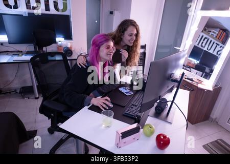 Two women collaborating on a project at a modern workspace with vibrant lighting Stock Photo