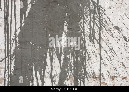 Grey cement splashes on white wall, close-up of liquid concrete drips on rough plaster texture, grunge architectural abstract background. Stock Photo
