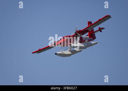 VICTORIA, VANCOUVER ISLAND, BC, CANADA – JUNE 18, 2025: A red Harbour Air twin-engine seaplane with pontoons flies overhead against a clear blue sky. Stock Photo