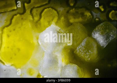 A horizontal studio macro photograph of melting ice cubes surrounded by pools and glistening drops of extra virgin olive oil on a white surface. Stock Photo