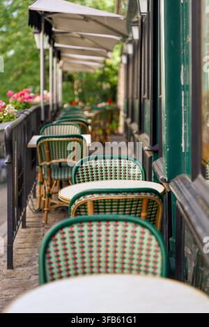 Empty woven chairs with distinctive green and white striped upholstery and small marble-topped tables recede into perspective beneath cream canvas awn Stock Photo