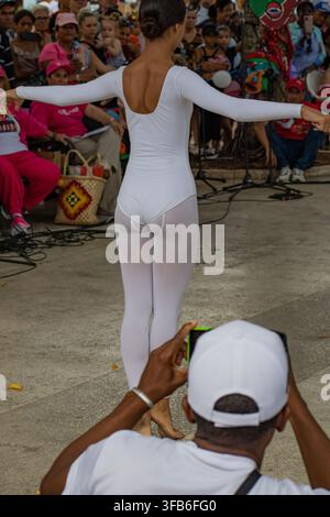 Man photographs a dancer performing in a white leotard at El Carnavalito in Ciego de Ávila, Cuba, on August 21, 2026. Stock Photo