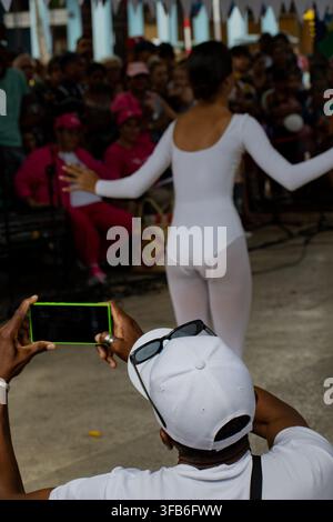 Man photographs a dancer performing in a white leotard at El Carnavalito in Ciego de Ávila, Cuba, on August 21, 2026. Stock Photo