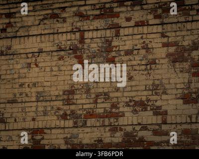 A weathered and aged brick wall texture with peeling tan and beige paint showing red brick beneath in an urban design Stock Photo