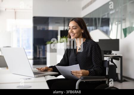 Confident businesswoman in wheelchair working remotely on laptop in office Stock Photo