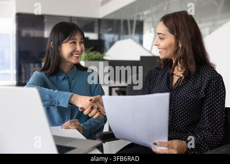 Woman sitting in wheelchair holding contract, handshaking with woman client Stock Photo