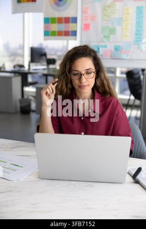 Focused businesswoman reviewing information, working on project using laptop Stock Photo