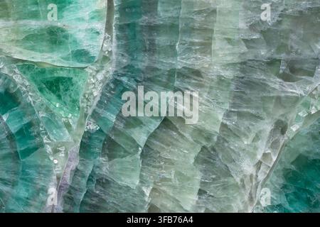 Macro view of a polished green fluorite slab revealing translucent crystalline layers, natural veining and shifting emerald, jade and grey mineral ton Stock Photo