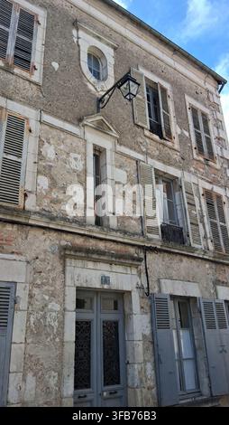 Weathered facade of a historic French townhouse with peeling plaster, grey shutters and ornate door in old town, France. Stock Photo