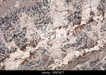 Close up of a polished white granite slab surface showing beige and grey mineral speckles with rust brown veining, a natural stone texture used for Stock Photo