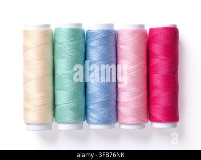Five spools of multi colored polyester sewing thread, side by side against plain white background. Colored sewing thread wound onto paper rolls. Stock Photo