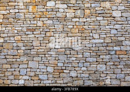 Rustic Natural Stone Wall Texture Background. Close view of a rustic wall built from irregular beige and gray stones, forming a detailed natural Stock Photo
