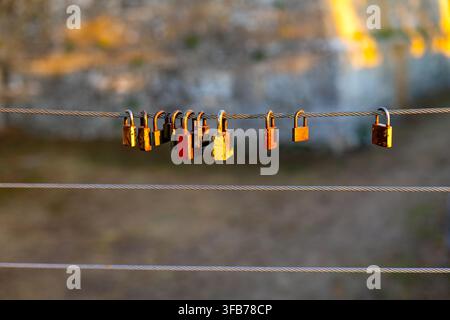 Colorful Love Padlocks Hanging on Steel Cable at Sunset. Colorful weathered padlocks hanging from a steel cable in warm golden sunlight with a softly Stock Photo