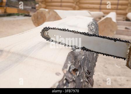 professional lumberjack saws logs, holding a chainsaw in his hand, to build wooden house. Stock Photo