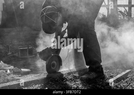 A worker builds a curb using various tools, including an angle grinder, in black and white Stock Photo