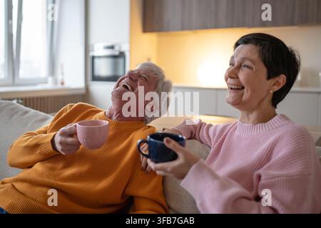 Happy senior couple at home together sitting on couch relaxing enjoying watching funny movie on tv. Stock Photo