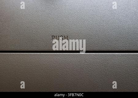 A close up of textured gray push button on simple mechanical panel, showing tactile surface detail, neutral color, horizontal seam, and functional ind Stock Photo