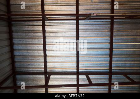 A corrugated metal roof with dark steel beam framework viewed from below in industrial building, creating geometric pattern of lines, texture, and nat Stock Photo