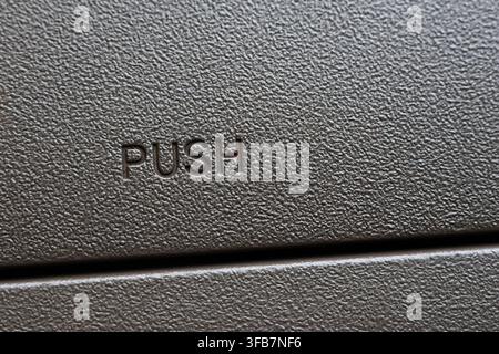 An embossed push button on textured black plastic panel showing simple industrial control surface with tactile detail and strong horizontal division Stock Photo
