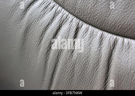 A gray leather upholstery texture with gathered seam detail, soft material surface and curved cushion closeup showing fine grain and tactile structure Stock Photo