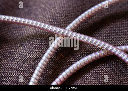 A macro photograph of metallic cord crossing over dark woven fabric, showing reflective texture, curved form, and detailed industrial surface under so Stock Photo
