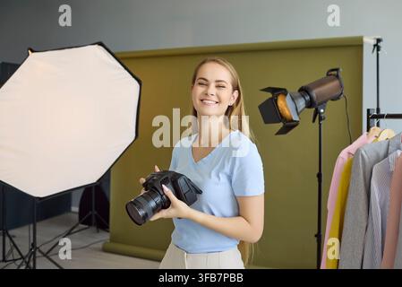 Happy woman photographer with DSLR in fashion studio, softbox and strobe lights Stock Photo