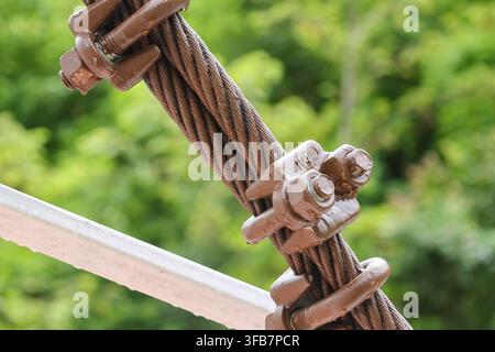 A rusty wire rope clamp with bolt on metal railing outdoors in green natural setting Stock Photo
