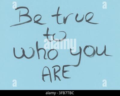 Handwritten message on light blue paper reads, "Be true to who you ARE," in black ink. The words are written in a casual, informal style. The message Stock Photo