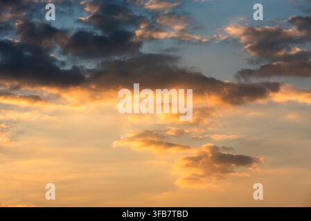 Beautiful evening sky during sunset with dramatic golden light illuminating soft cumulus clouds beneath dark stormy cloud formations. Stock Photo