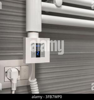 Close-up of a digital temperature controller installed on an electric heated towel rail in a modern bathroom, showing adjustable heating controls and Stock Photo