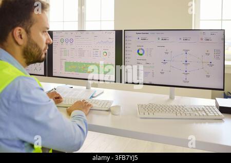 Engineer analyzing data on dual computer screens in industrial control room Stock Photo