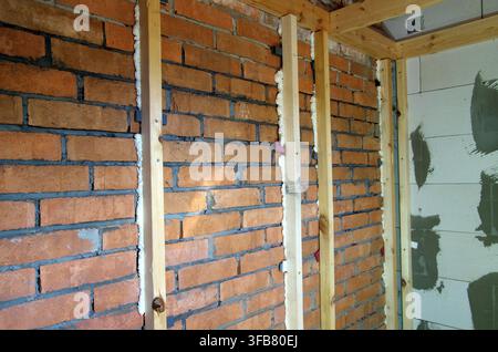 An indoor shot showing the process of interior wall insulation or leveling. Vertical wooden timber studs are mounted onto an old red brick wall and se Stock Photo