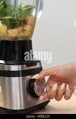 female hands preparing fresh vegetable smoothie and turn on electric blender. close-up Stock Photo