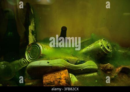 The lakebed is polluted with a heap of trash—including a moldy shoe, rusty cans, and bottles—causing total environmental degradation. Stock Photo