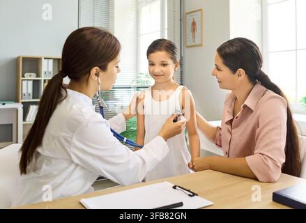 Pediatrician using stethoscope to examine child with mother during clinic visit Stock Photo