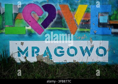 Colorful "Love Mrągowo" Graffiti Mural on Weathered Wall With Bold Typography and Peeling Paint - The town of Mrągowo in Masuria. Stock Photo