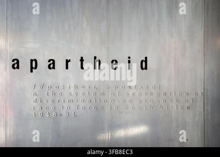 The dictionary definition of apartheid embossed on a metal and concrete wall exhibit, detailing the historical system of racial segregation Stock Photo