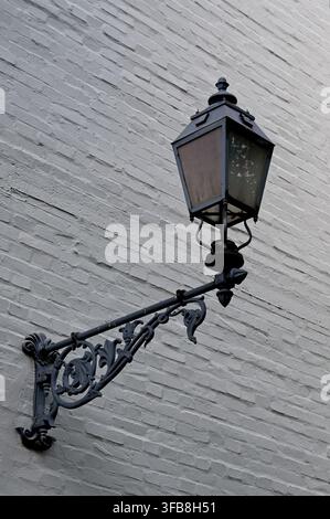Classic wrought iron vintage street lamp lantern mounted on a white brick wall facade. Stock Photo