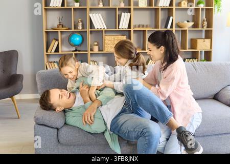 Playful parents and children tickling at home on sofa, cheerful family fun Stock Photo