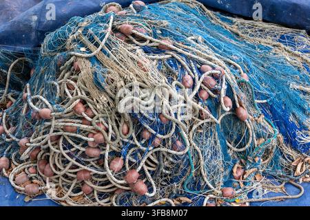 Tangled fishing nets and ropes lie piled together on a blue tarp. Stock Photo