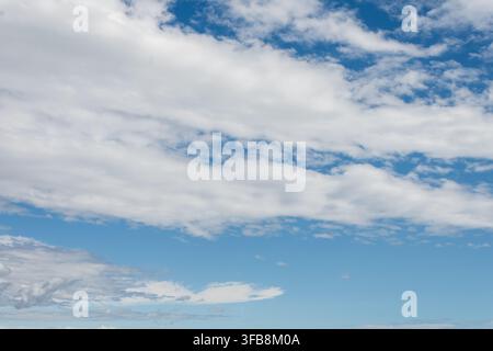 Bright blue sky is filled with soft white clouds across the frame. Stock Photo